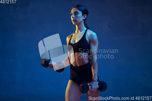 Image of Caucasian young female athlete practicing on blue studio background in neon light