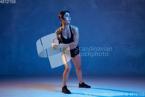 Image of Caucasian young female athlete practicing on blue studio background in neon light