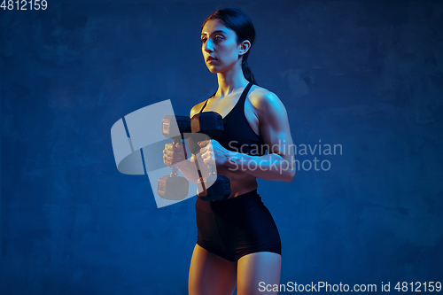 Image of Caucasian young female athlete practicing on blue studio background in neon light