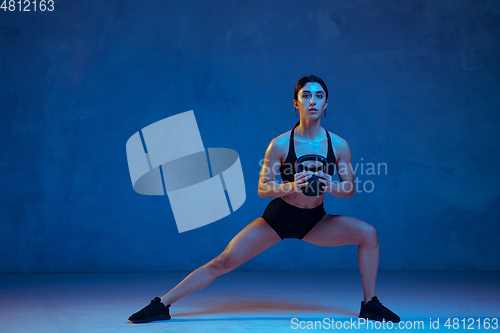 Image of Caucasian young female athlete practicing on blue studio background in neon light