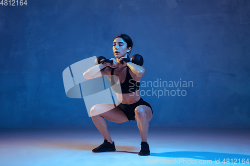 Image of Caucasian young female athlete practicing on blue studio background in neon light