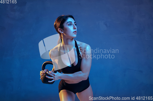 Image of Caucasian young female athlete practicing on blue studio background in neon light