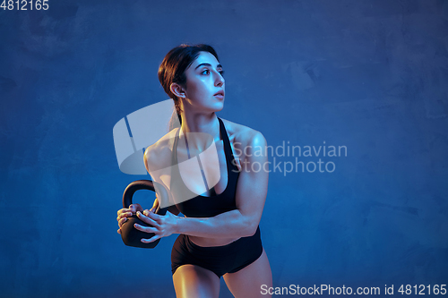 Image of Caucasian young female athlete practicing on blue studio background in neon light