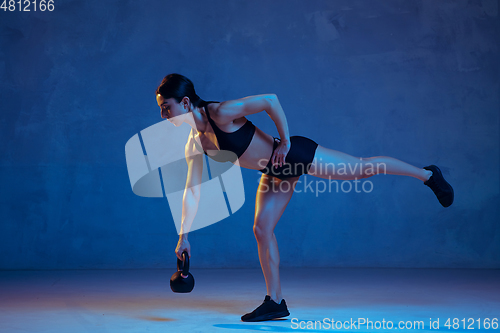 Image of Caucasian young female athlete practicing on blue studio background in neon light