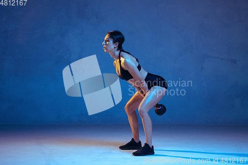 Image of Caucasian young female athlete practicing on blue studio background in neon light