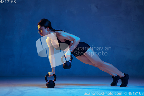 Image of Caucasian young female athlete practicing on blue studio background in neon light