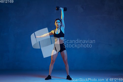 Image of Caucasian young female athlete practicing on blue studio background in neon light