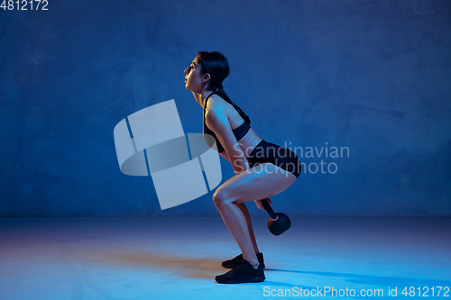 Image of Caucasian young female athlete practicing on blue studio background in neon light