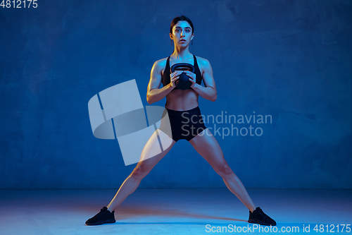 Image of Caucasian young female athlete practicing on blue studio background in neon light