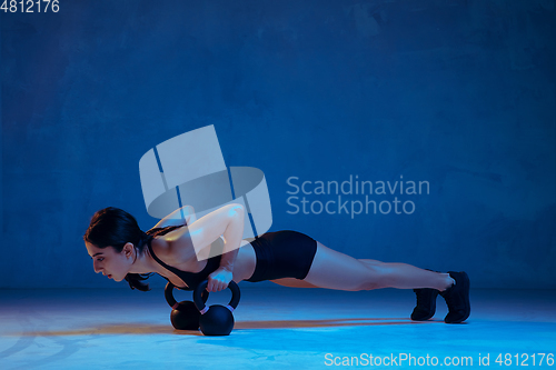 Image of Caucasian young female athlete practicing on blue studio background in neon light