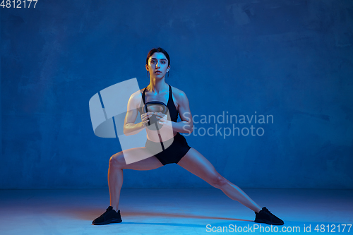 Image of Caucasian young female athlete practicing on blue studio background in neon light