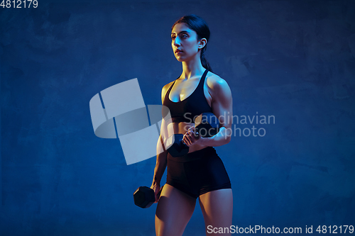 Image of Caucasian young female athlete practicing on blue studio background in neon light