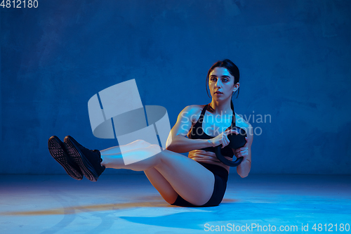 Image of Caucasian young female athlete practicing on blue studio background in neon light