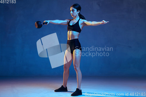 Image of Caucasian young female athlete practicing on blue studio background in neon light