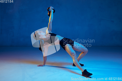 Image of Caucasian young female athlete practicing on blue studio background in neon light