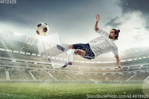 Image of Male soccer, football player catching ball in jump at the stadium during sport match on dark sky background