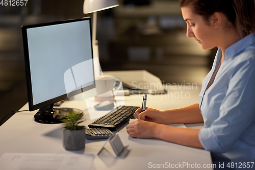 Image of businesswoman writing to notebook at night office