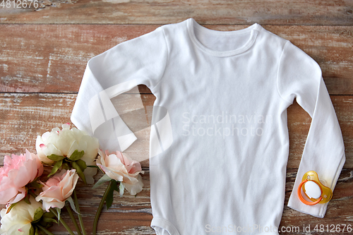 Image of baby bodysuit with soother and flowers on wood