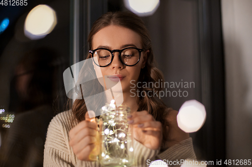 Image of woman with garland lights in glass mug at home