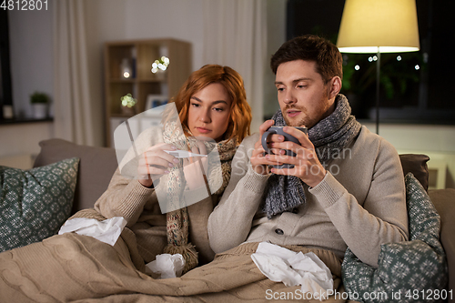 Image of sick couple with thermometer and tea at home