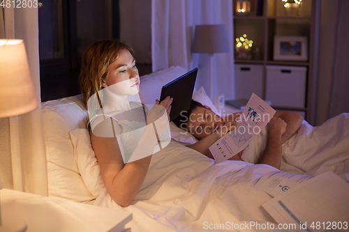 Image of woman with tablet computer working in bed at night