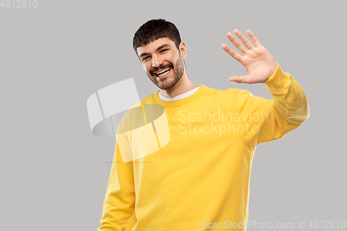 Image of smiling young man in yellow sweatshirt waving hand