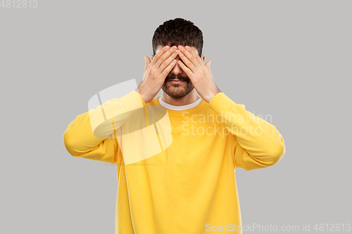 Image of man in yellow sweatshirt closing his eyes by hands