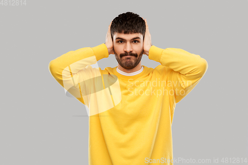 Image of man in yellow sweatshirt closing ears by hands