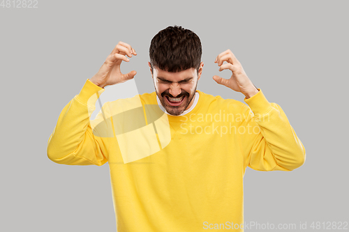 Image of angry young man in yellow sweatshirt over grey