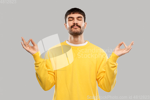 Image of young man in yellow sweatshirt meditating