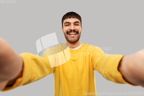 Image of happy young man in yellow sweatshirt making selfie