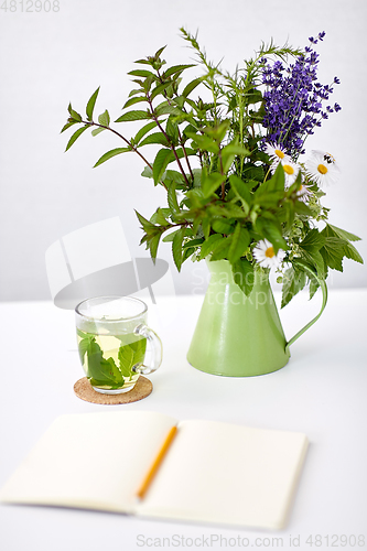 Image of herbal tea, notebook and flowers in jug on table