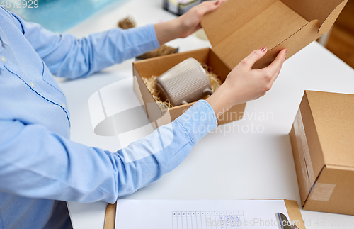 Image of woman packing mug to parcel box at post office