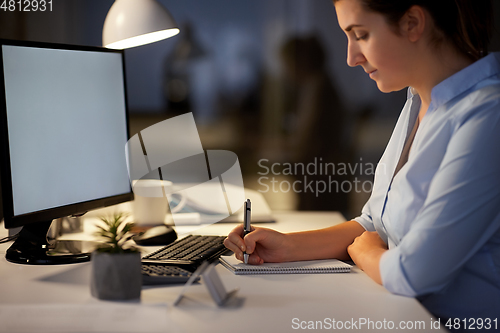 Image of businesswoman writing to notebook at night office