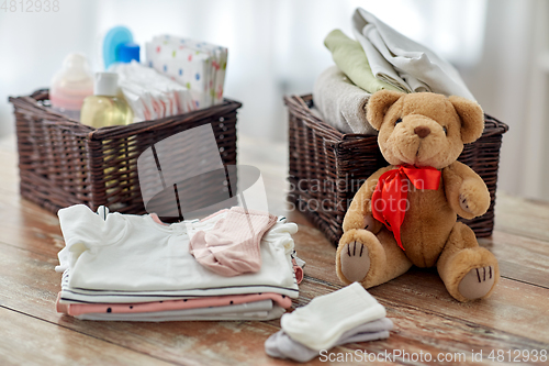 Image of baby clothes and teddy bear toy on table at home