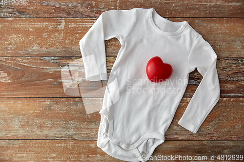 Image of baby bodysuit with red heart toy on wooden table