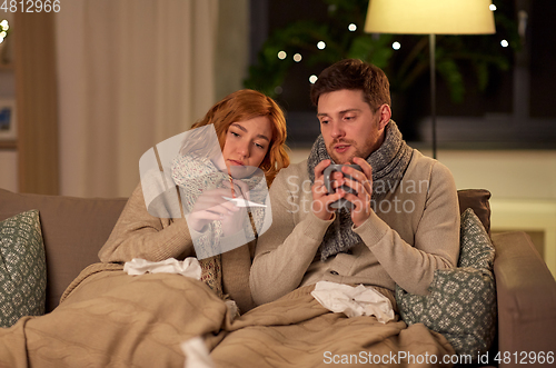 Image of sick couple with thermometer and tea at home