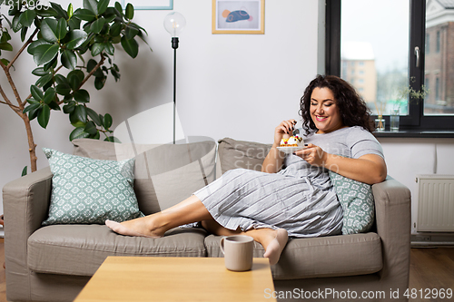 Image of smiling young woman eating cake at home