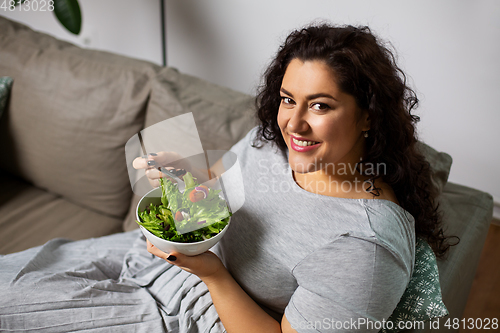 Image of smiling young woman eating vegetable salad at home