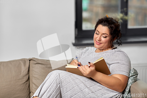 Image of happy young woman with diary on sofa at home