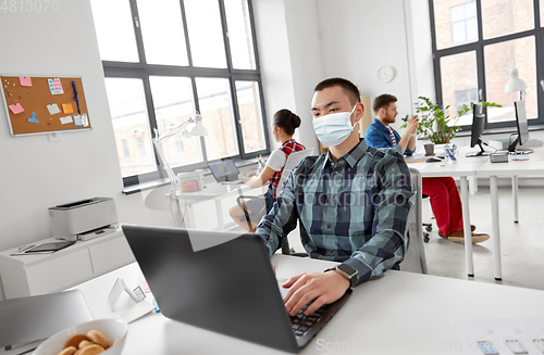 Image of man in medical mask with laptop working at office