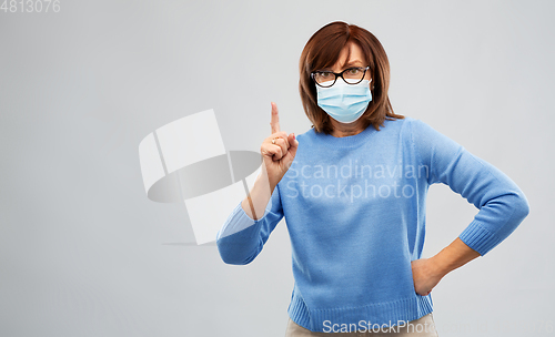 Image of senior woman in medical mask pointing finger up