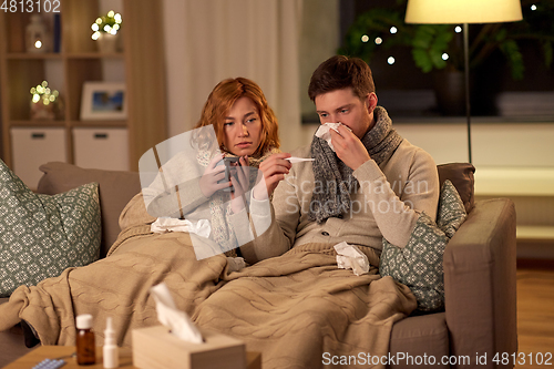 Image of sick couple with thermometer and tea at home