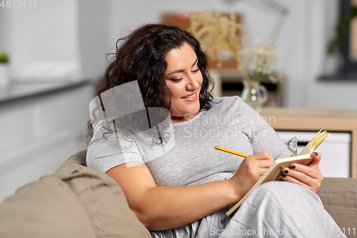 Image of happy young woman with diary on sofa at home