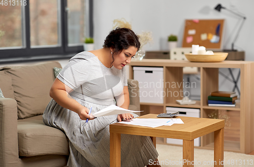 Image of woman with bills or papers and calculator at home