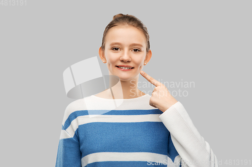 Image of smiling teenage girl pointing finger to her face