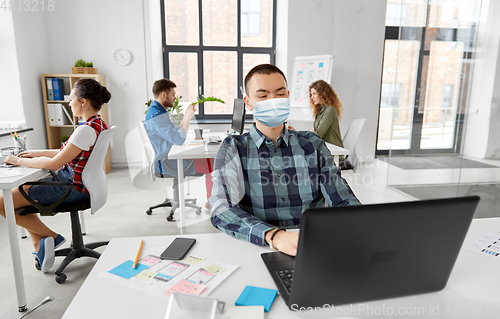 Image of man in medical mask with laptop working at office