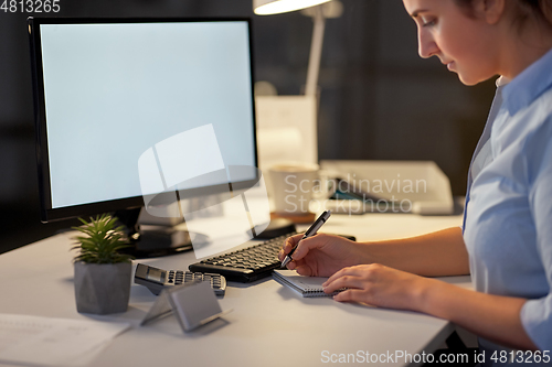 Image of businesswoman writing to notebook at night office