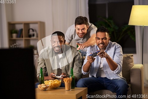 Image of happy friends playing video games at home at night