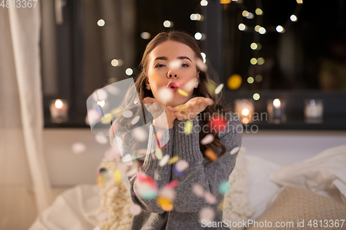 Image of woman blowing confetti from her hands at home